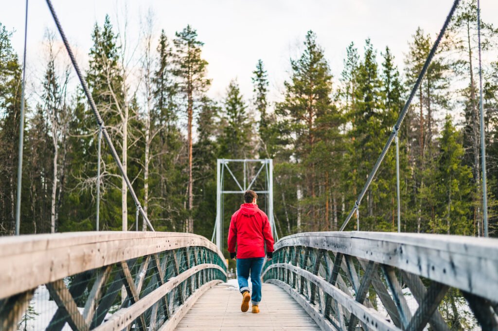 Man walking on a wooden bridge towards a forest on an independent hike from Rovainemi
